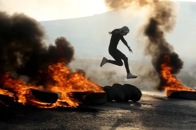 Palestinian man jumps over burning tires as people protest over tensions in Jerusalem's Al-Aqsa Mosque, at Huwara checkpoint, near Nablus in the Israeli-occupied West Bank on May 29, 2022. (Photo by Raneen Sawafta/Reuters)