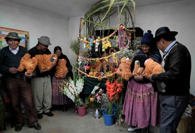 The Ali and Rios family hold traditional “Tantawawas”, bread shaped as children, as they stand next to a table with offerings for their dearly departed, during Day of the Dead celebrations in El Alto, Bolivia, Monday, November 1, 2021. (Photo by Juan Karita/AP Photo)