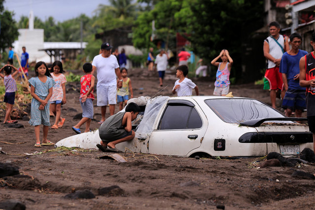 Residents look at a car buried by volcanic ash which cascaded into a village triggered by heavy rains brought about by Tropical Storm Trami at a village in Guinobatan town, Albay province South of Manila on October 23, 2024. Torrential rains driven by the storm have turned streets into rivers, submerged entire villages and buried some vehicles up to their door handles in volcanic sediment knocked loose by the downpour. (Photo by Charism Sayat/AFP Photo)