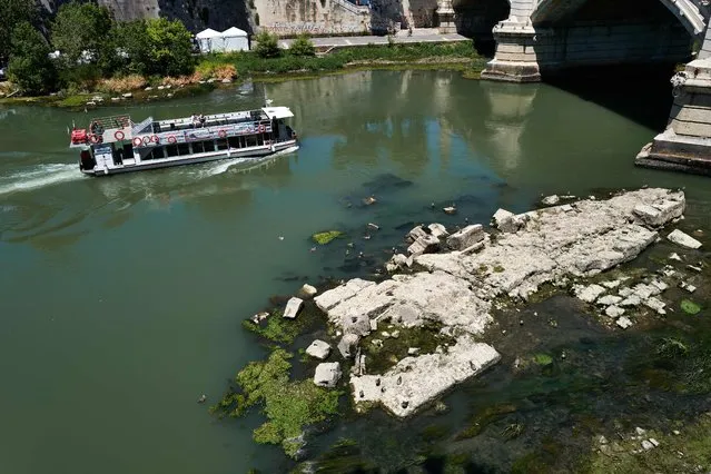 This picture taken on July 2, 2022 in Rome shows a tourist river boat sailing near the Vittorio Emanuele II bridge, as the low water level of the river Tiber reveals an ancient bridge built under Roman Emperor Nero (Bottom R). (Photo by Andreas Solaro/AFP Photo)