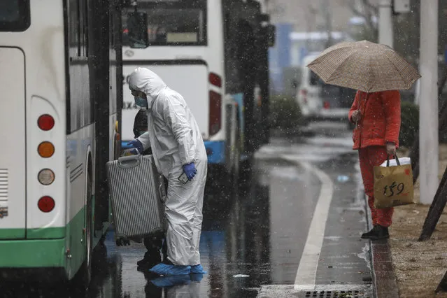 A worker wearing a protective suit helps a patient carry their luggage as they arrive at a tumor hospital newly designated to treat COVID-19 patients in Wuhan in central China's Hubei Province, Saturday, February 15, 2020. The virus is thought to have infected more than 67,000 people globally and has killed at least 1,526 people, the vast majority in China, as the Chinese government announced new anti-disease measures while businesses reopen following sweeping controls that have idled much of the economy. (Photo by Chinatopix via AP Photo)