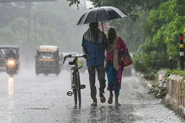 A couple shares an umbrella during a rain shower on the outskirts of New Delhi on July 12, 2022. (Photo by Prakash Singh/AFP Photo)