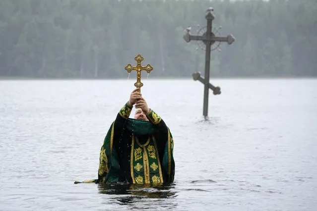 An Orthodox priest blesses water prior to a traditional pilgrim's swim around a cross, which marks St. Antony Dymsky of the Russian Orthodox Church in Dymskoye lake near Antonyevo-Dymsky Holy Trinity Monastery, 230 kilometers (143 miles) south-east from St. Petersburg, Russia, Thursday, July 7, 2022. The saint, who lived in this place in 13th century, used to spend several hours daily while standing and praying on the underwater stone in the lake. (Photo by Dmitri Lovetsky/AP Photo)