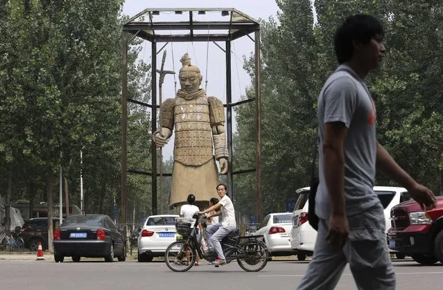 A woman rides a bicycle past a large replica of a Terracotta Warrior sculpture at a park on the outskirts of Beijing August 21, 2014. (Photo by Jason Lee/Reuters)
