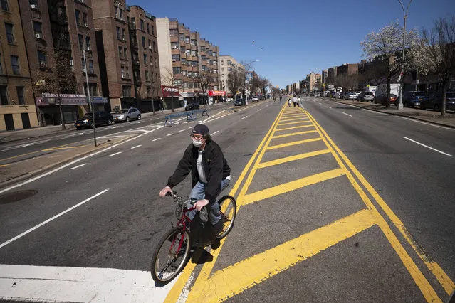 A man wearing a mask bicycles along a section of the Grand Concourse that has been temporarily closed to vehicular traffic as the city tests out a pilot program providing more social distancing space during the coronavirus pandemic, Friday, March 27, 2020 in the Bronx borough of New York. (Photo by Mark Lennihan/AP Photo)