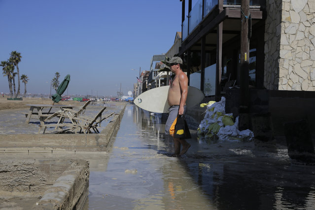A man carries his board as he walks through the flooded beachfront properties, Wednesday, August 27, 2014, in Seal Beach, Calif. A low-lying street in the Southern California coastal community of Seal Beach has been inundated by a surge of rising seawater brought on by Hurricane Marie spinning off Mexico's Pacific coast. (Photo by Jae C. Hong/AP Photo)