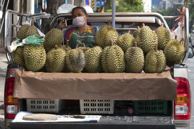 A fruit vendor wearing a face mask to protect from the new coronavirus talks on a mobile phone near durian on her van in Bangkok, Thailand, Thursday, April 23, 2020. (Photo by Sakchai Lalit/AP Photo)