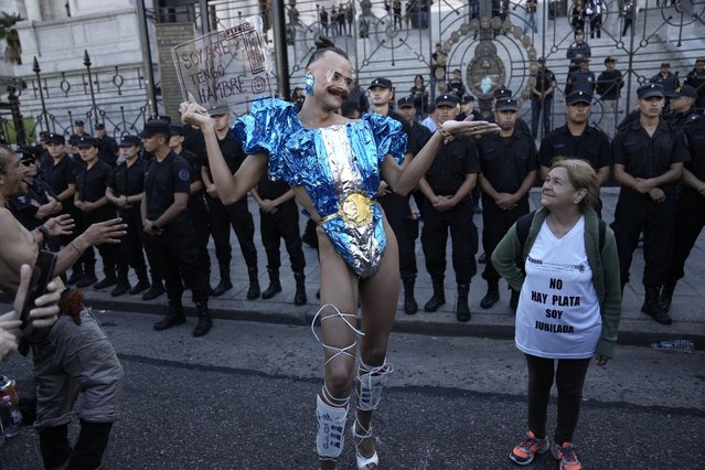 Vick Teker, dressed in a national flag outfit holding a sign with a message that reads in Spanish: “I am art and I am hungry”, and a woman wearing a T-shirt with a message that reads: “There is no money. I am retired”, take part in a demonstration outside Congress as part of a national strike to protest the economic and labor reforms proposed by Argentine President Javier Milei in Buenos Aires, Argentina, Wednesday, January 24, 2024. (Photo by Rodrigo Abd/AP Photo)