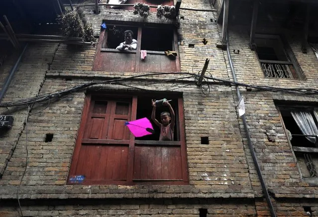 A Nepalese child flies a kite from a window on the ocassion of the Dashain festival in Bhaktapur, on the outskirts of Kathmandu on October 2, 2014.  Dashain is the longest and the most auspicious festival in the Nepalese calendar and celebrates the triumph of good over evil. (Photo by Prakash Mathema/AFP Photo)