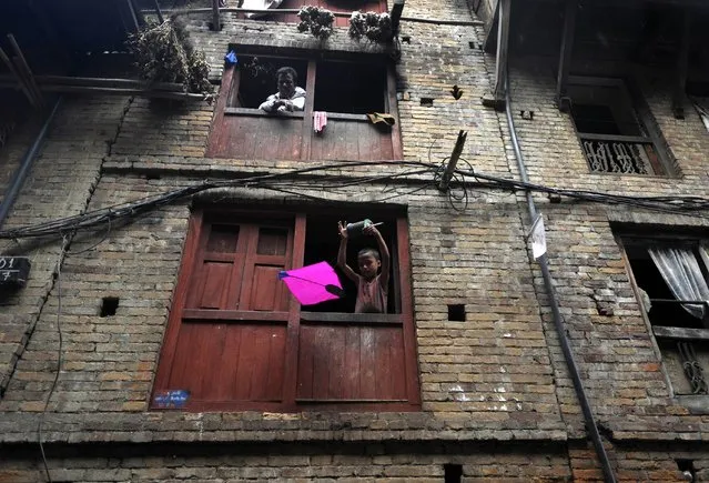 A Nepalese child flies a kite from a window on the ocassion of the Dashain festival in Bhaktapur, on the outskirts of Kathmandu on October 2, 2014. Dashain is the longest and the most auspicious festival in the Nepalese calendar and celebrates the triumph of good over evil. (Photo by Prakash Mathema/AFP Photo)