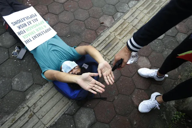 A protester uses a hand sanitizer as he lies on the ground demanding better handling of the COVID-19 pandemic in Kathmandu, Nepal, Saturday, June 20, 2020. Hundreds participated demanding increased testing and protesting alleged corruption by government officials while purchasing equipment and testing kits. (Photo by Niranjan Shrestha/AP Photo)