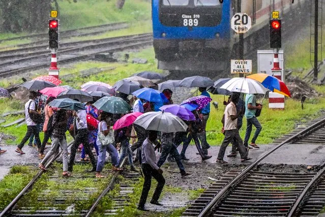 Pedestrians carrying umbrellas walk along a railway crossing during heavy downpour in Colombo on October 21, 2022. (Photo by Ishara S. Kodikara/AFP Photo)