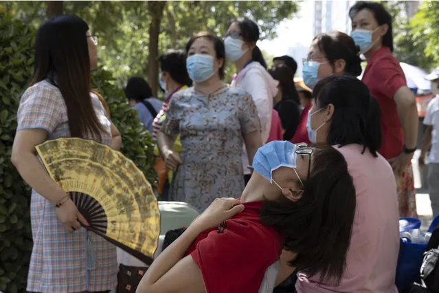 Parents wearing masks to curb the spread of the coronavirus wait in the shade as their children take part in their college entrance exams in Beijing, China on Tuesday, July 7, 2020. Almost 11 million students began taking China's university entrance exam Tuesday after a delay as the country worked to bring down coronavirus infections. (Photo by Ng Han Guan/AP Photo)