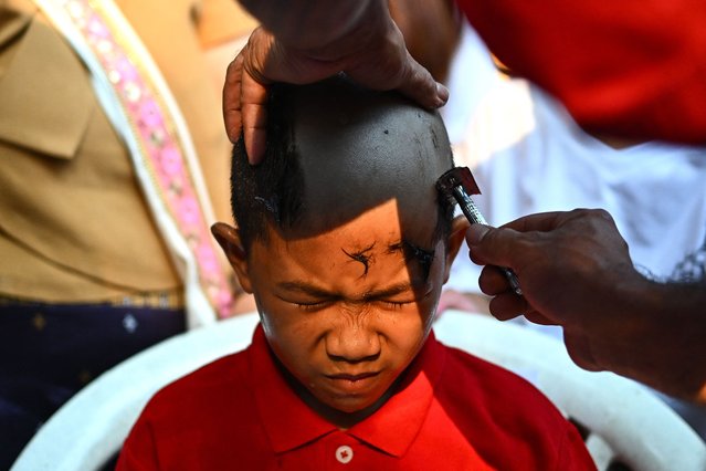 This photograph taken on March 27, 2025 shows nine-year-old Donlaphat Lungta, an ethnic Shan boy getting his head shaved by a Buddhist monks on the eve of the annual Poy Sang Long procession a traditional rite of passage ceremony for young boys to be initiated as novice Buddhist monks at the Wat Ku Tao Buddhist temple in Chiang Mai in northern Thailand. (Photo by Manan Vatsyayana/AFP Photo)