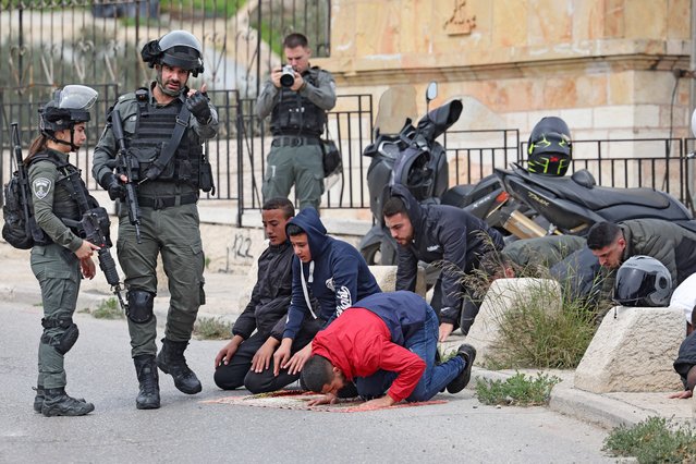 Israeli security forces stand guard as Palestinian Muslims perform the Friday Noon prayer on a street in east Jerusalem on February 23, 2024, as age restrictions have been imposed to access the Al-Aqsa Mosque compound, amid the ongoing battles between Israel and the Palestinian group Hamas. (Photo by Ahmad Gharabli/AFP Photo)