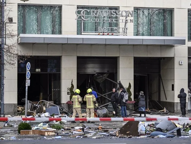 Fire fighters stand in front of a hotel after a burst and leak of the AquaDom aquarium in Berlin, Germany, 16 December 2022. A 14-meter aquarium has burst at a hotel in downtown Berlin, injuring two people, German rescue services said. The home to around 1,500 exotic fish spills 1 million liters of water and floats a major road in the Mitte district, emergency services said. (Photo by Filip Singer/EPA/EFE)