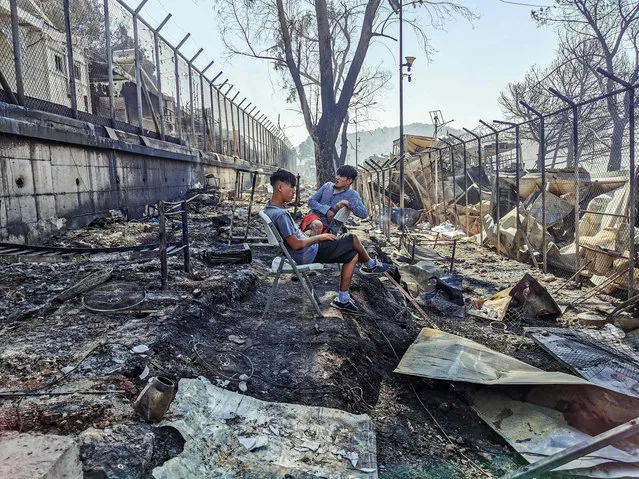 Migrants sit inside the burnt Moria Camp on the Greek island of Lesbos on September 9, 2020, after a major fire. Thousands of asylum seekers on the Greek island of Lesbos fled for their lives early September 9, as a huge fire ripped through the camp of Moria, the country's largest and most notorious migrant facility. Over 12,000 men, women and children ran in panic out of containers and tents and into adjoining olive groves and fields as the fire destroyed most of the overcrowded, squalid camp. The blaze started just hours after the migration ministry said that 35 people had tested positive at the camp. (Photo by Anthi Pazianou/AFP Photo)