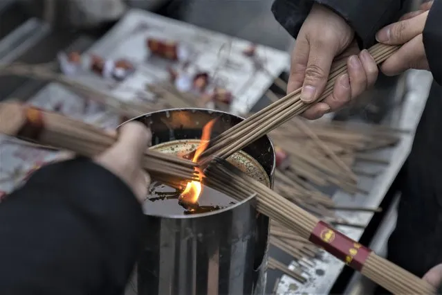 Visitors light incense as they pray on the first day of the Lunar New Year holiday at the Lama Temple in Beijing, Sunday, January 22, 2023. (Photo by Mark Schiefelbein/AP Photo)