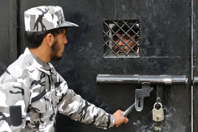 A member of Taliban security force stands guard as an inmate watches from behind the closed gate of a prison in Jalalabad on January 19, 2023. (Photo by Shafiullah Kakar/AFP Photo)