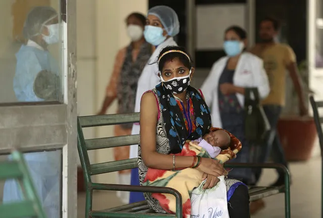 A woman wearing a face mask waits with an infant at a government- run hospital in Jammu, India, Monday, October 5, 2020. India, the second worst-affected nation in the world after the United States, is witnessing a sustained decline in new coronavirus infections and active virus cases have remained below the million mark for 14 consecutive days. (Photo by Channi Anand/AP Photo)