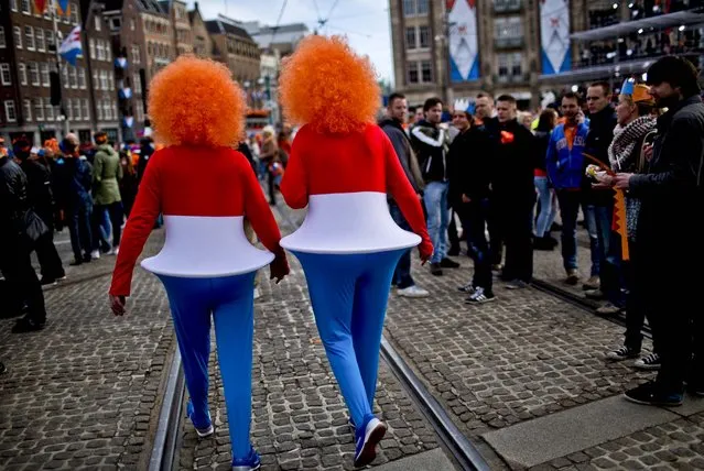 Two men walk in Dam Square as they arrive outside the Royal Palace in downtown Amsterdam, The Netherlands, on April 30, 2013. Around a million people are expected to descend on the Dutch capital for a huge street party to celebrate the first new Dutch monarch in 33 years. (Photo by Emilio Morenatti/Associated Press)