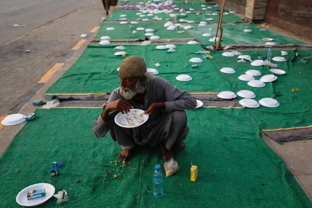 A man sits with empty plates as he eats boiled rice after breaking his fast at an event organised by a charity organisation, during the fasting month of Ramadan, along a sidewalk in Karachi, Pakistan on March 29, 2023. (Photo by Akhtar Soomro/Reuters)