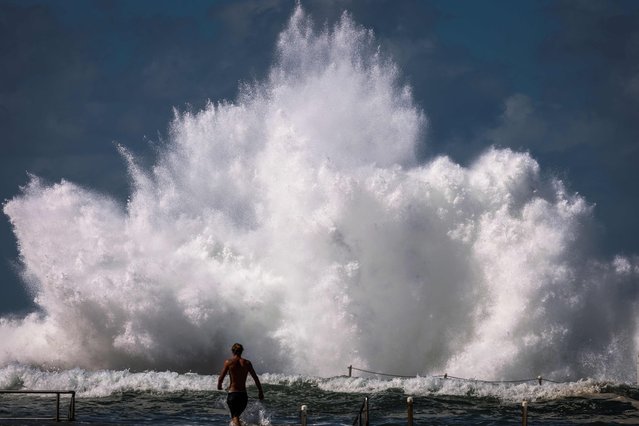 A man walks towards a wave breaking on a rock pool at North Narrabeen Beach in Sydney on April 18, 2025, as large swells hit the east coast of Australia. (Photo by David Gray/AFP Photo)