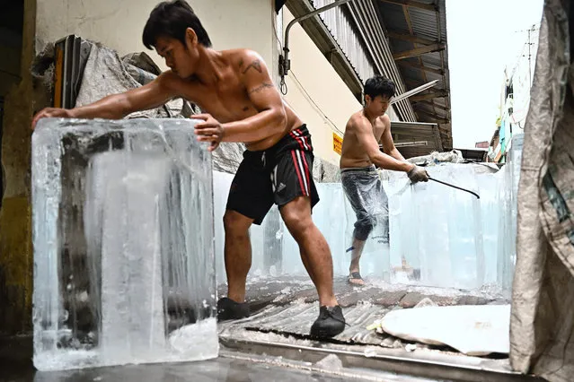 Workers move blocks of ice into a storage unit at a fresh market during heatwave conditions, in Bangkok on April 25, 2023. (Photo by Lillian Suwanrumpha/AFP Photo)