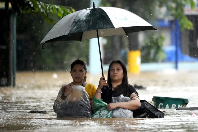 Residents protect their belongings as they negotiate a flooded street caused by heavy rains from Tropical Storm Yagi, locally called Enteng, in Cainta, Rizal province, Philippines, Monday, September 2, 2024. (Photo by Aaron Favila/AP Photo)