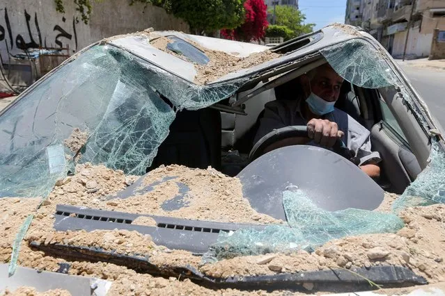 A Palestinian man drives his car, which was damaged in an Israeli air strike, as he heads to a garage, in Gaza City on May 19, 2021. (Photo by Ibraheem Abu Mustafa/Reuters)