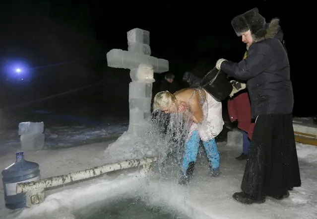 A priest pours icy water over a woman during celebrations for the Orthodox Epiphany on the ice-covered Mana river, with the air temperature at about minus 33 degrees Celsius (minus 27.4 degrees Fahrenheit), in Taiga area near the Siberian village of Mansky outside Krasnoyarsk, Russia, January 19, 2016. (Photo by Ilya Naymushin/Reuters)