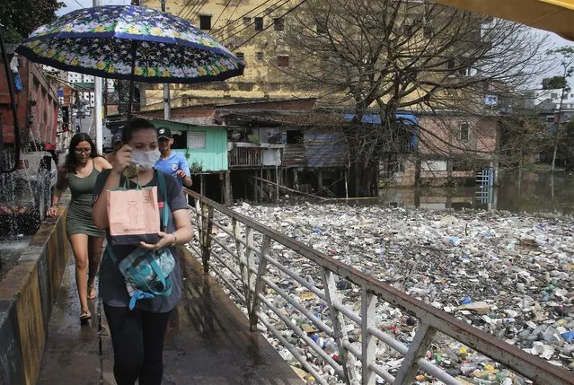 People cross a bridge next to accumulated garbage floating on the rising course of the Negro River, in Manaus, Amazonas state, Brazil, Monday, June 06, 2022. According to local authorities, about 35 tons of garbage are being removed daily from the water in Manaus. (Photo by Edmar Barros/AP Photo)