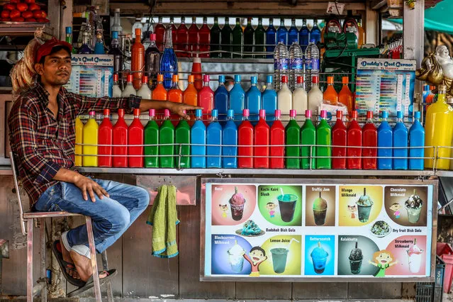 An Indian street food vendor waits for customers seated next to a row of brightly colored syrup bottles at his street Gola (Shaved Ice) stall, at Girgaon Chowpaty in Mumbai, India, 23 October 2018. Gola (shaved ice) or barf ka gola or chuski are the most popular street desserts. The ice-based dessert is made by shaving an ice-block and pouring various flavored syrups to the snow-like crushed ice. Street food in Asia is a bit of everything that delights the palate and comes at a good price. It is colorful, tasty and varied; sometimes sharp, saucy or spicy. There is something for the sweet tooth, or to suit those looking more for a savory sensation. Drinks and snacks and full meals. (Photo by Divyakant Solanki/EPA/EFE)