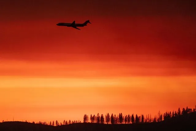 This photograph taken on July 25, 2022, shows a firefighting jet air tanker flying through a smoky sunset sky during the Oak Fire near Mariposa, California, burning west of Yosemite National Park where the Washburn Fire has threatened the giant sequoia trees of the Mariposa Grove. Firefighters were battling California's largest wildfire of the summer on July 25, 2022, a blaze near famed Yosemite National Park that has forced thousands of people to evacuate, officials said, as the Oak Fire in Mariposa County has engulfed 16,791 acres (6.795 hectares) and is 10 percent contained, Cal Fire, the state fire department, said. (Photo by David McNew/AFP Photo)
