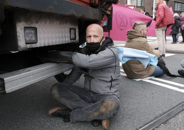 An activist chained himself to a tube while protestors from climate activism group of Extinction Rebellion block a busy intersection near the temporary home of the Dutch parliament in The Hague, Netherlands, Monday, October 11, 2021. The group says it plans a series of demonstrations in the city throughout the week ahead of a major United Nations climate conference that opens Oct. 31, in Glasgow. (Photo by Patrick Post/AP Photo)