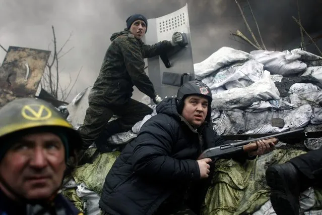 An anti-government protester holds a firearm as he mans a barricade on the outskirts of Independence Square in Kiev, Ukraine, Thursday, February 20, 2014. (Photo by Marko Drobnjakovic/AP Photo)