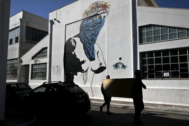 Two men carry a painting as they make their way past graffiti “Athena vs Europa, Resist vs Submit”, which depicts the ancient statue of Goddess Aphrodite of Milo wearing a scarf and a wreath consisting of the stars of the European Union flag, made by French street artist Goin in Athens May 25, 2015. (Photo by Alkis Konstantinidis/Reuters)