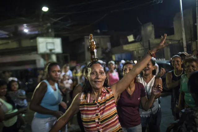 In this Sunday, May 19, 2019 photo, a woman jokes around with a full bottle of beer on her head as she celebrates winning the dancing contest at a Mother's Day block party in Caracas, Venezuela. Although Mother's Day was officially celebrated the previous weekend, people in the Petare area organized the neighborhood party to celebrate the mothers of their community. (Photo by Rodrigo Abd/AP Photo)