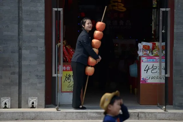 A sales woman holds a string of apple models as she waits for customers at the entrance of a shop in Beijing on April 7, 2014. China has announced a set of steps to boost slowing growth in the world's number-two economy, including extending tax breaks for small businesses and support measures for poor urban districts. (Photo by Wang Zhao/AFP Photo)