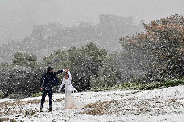 A newlywed couple from the US enjoys a snowfall during a photo shooting near the Acropolis in Athens on January 24, 2022. Schools are closed in greatest Athens area, as Greece exepriences a cold.weather front with heavy snowfalls and very low temperatures. (Photo by Louisa Gouliamaki/AFP Photo)