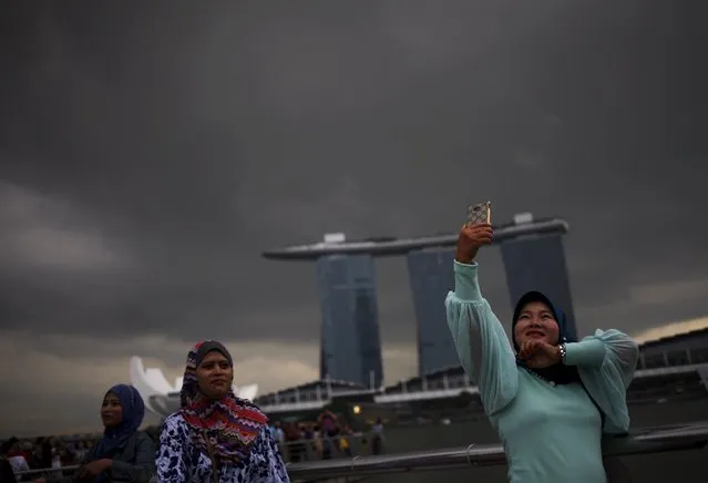 An Indonesian tourist poses for photos as storm clouds gather at the Merlion Park in Singapore May 14, 2015. (Photo by Edgar Su/Reuters)