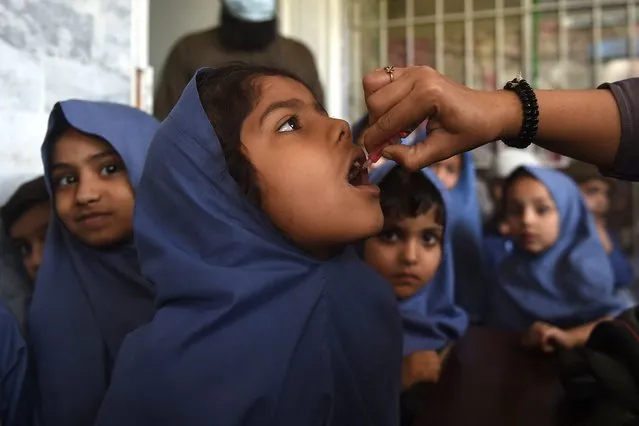A health worker administers polio vaccine drops to a young girl as others wait for their turn at a school during a door-to-door polio vaccination campaign in Karachi on February 28, 2022. (Photo by Rizwan Tabassum/AFP Photo)