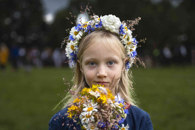 A girl wearing a crown made of flowers takes part in the Saint John's Day and summer solstice celebration in the small town of Kernave, some 35km (22 miles) northwest of the capital, Vilnius, Lithuania, on Sunday, June 23, 2024.  St. John's Day, or Midsummer Day, the shortest night of the year, is celebrated with festivities that include making oak leaf wreaths, leaping over flames, and encouraging young people to go out and look for fern flowers. (Photo by Mindaugas Kulbis/AP Photo)