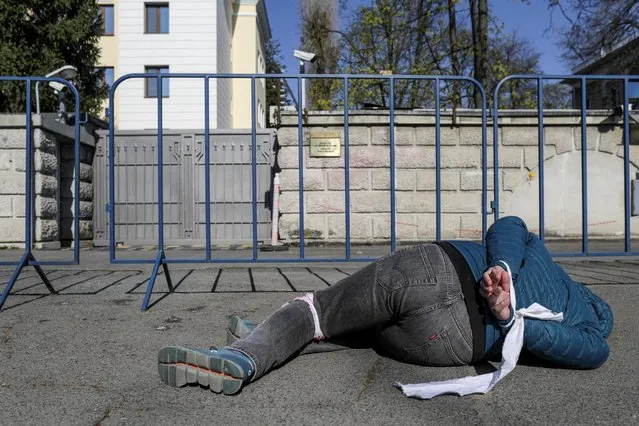 Romanian activist Mihail Bumbes lies on the sidewalk in front of the Russian Embassy in Bucharest with his hands tied behind his back and with red-died pieces of cloth and red paint on the back of his hand depicting the posture of a civilian found dead in Bucha, Ukraine, in Bucharest, Romania on April 5 2022. (Photo by Octav Ganea/Inquam Photos via Reuters)