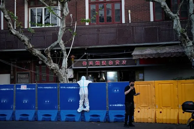 A person in a protective suit looks over barricades set around a sealed-off area, during a lockdown to curb the spread of the coronavirus disease (COVID-19) in Shanghai, China on April 11, 2022. (Photo by Aly Song/Reuters)