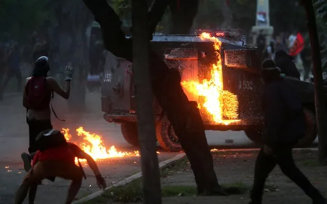 Demonstrators run near a riot police vehicle which has been set on fire during a protest against Chile's government in Santiago, Chile on December 18, 2019. (Photo by Ricardo Moraes/Reuters)
