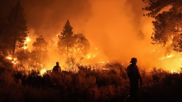 Two firefighters watch the Bridge Fire burn near a structure in Wrightwood, Calif., Tuesday, September 10, 2024. (Photo by Jae C. Hong/AP Photo)