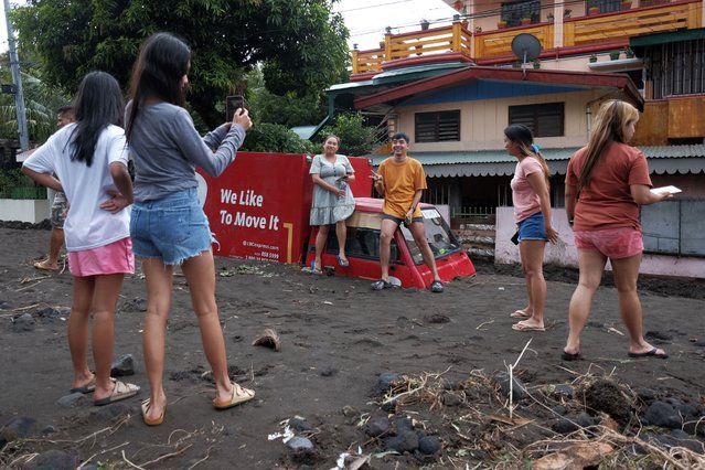 Residents pose beside a delivery van buried by volcanic mud that flowed down from Mayon volcano after heavy rains caused by Tropical Storm Trami hit Guinobatan town, Albay province, Philippines on Wednesday October 23, 2024. (Photo by John Michael Magdasoc/AP Photo)