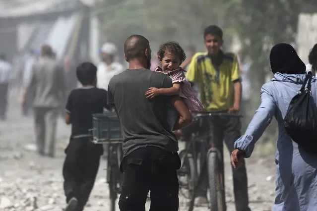 A man carries a girl reacting at a site hit by what activists said were air strikes by forces loyal to Syria's President Bashar al-Assad on a marketplace in the Douma neighborhood of Damascus, Syria August 16, 2015. (Photo by Bassam Khabieh/Reuters)