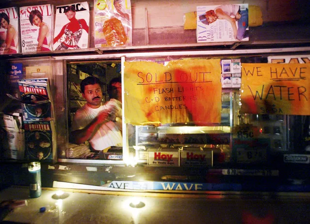 A vendor stands in his candlelit store window with signs reading “We Have Water” and “Sold Out Flashlights Batteries Candles” during a massive blackout August 15, 2003 in New York City. Power is slowly returning to certain parts of the city. (Photo by Mario Tama/Getty Images)